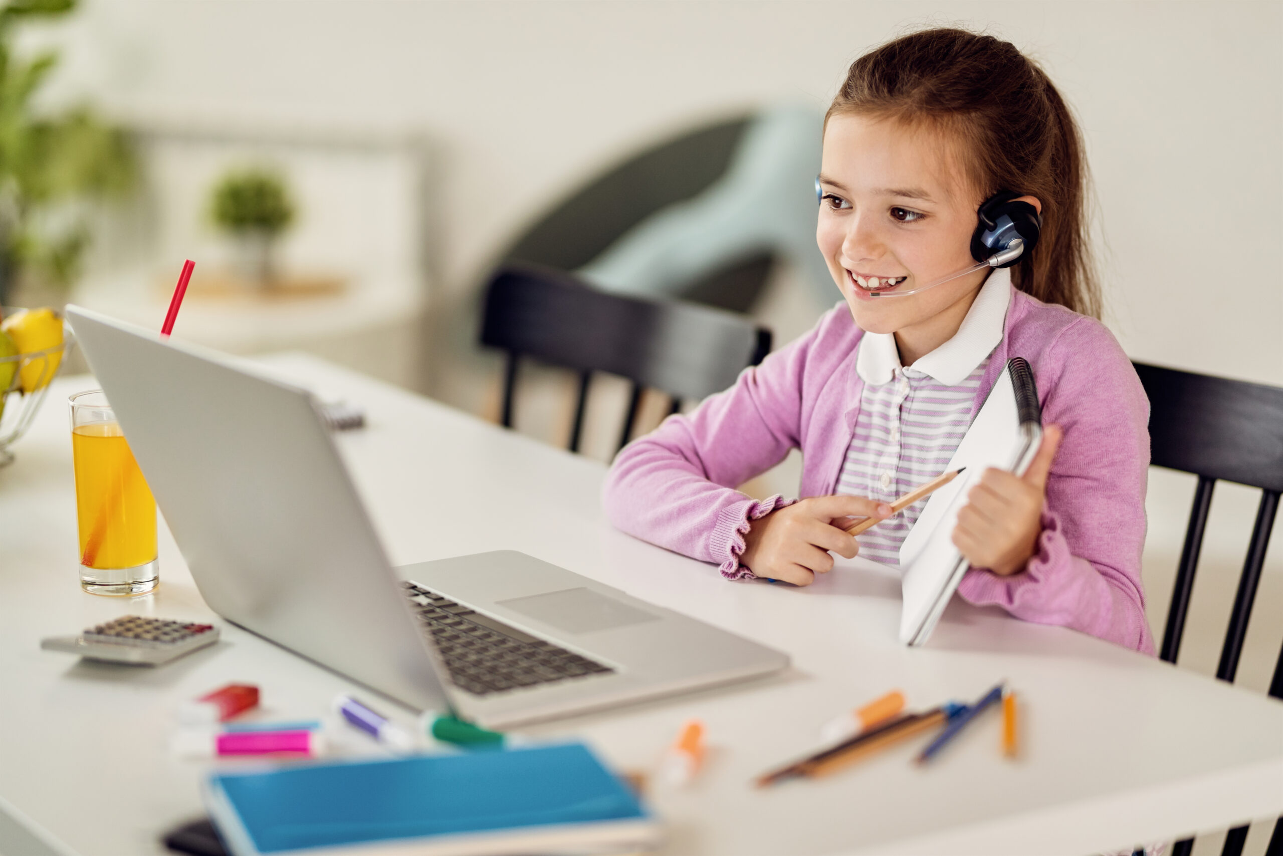 Happy girl using computer and talking to her teacher via video call while learning at home.